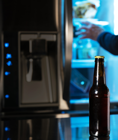 A young man steals beer from the fridge. 