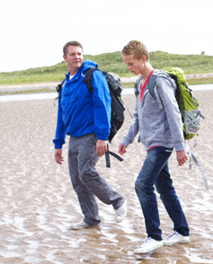 Dad and son walk on the beach as they talk.