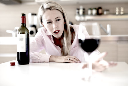 Young blond woman reaching for glass of wine—addiction.