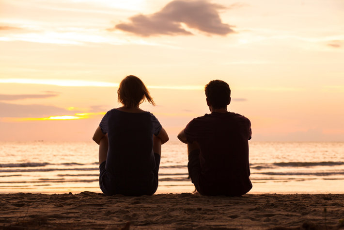 Two people sitting on the beach in a sunshine.