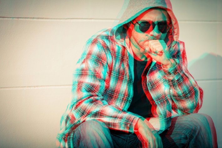 Fuzzy image of the addict sitting in sunglasses and hoodie.