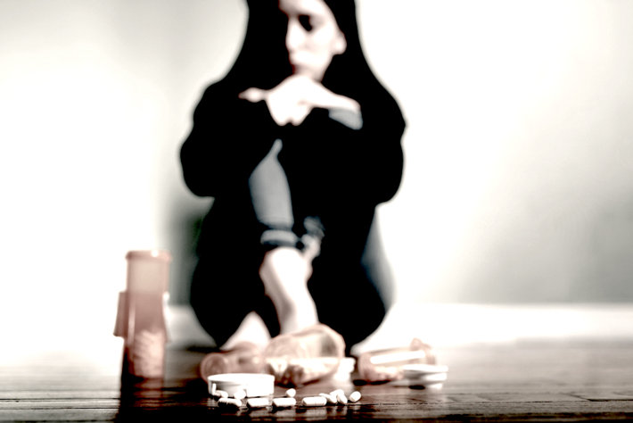 Addict girl sitting on the floor with prescription medication.
