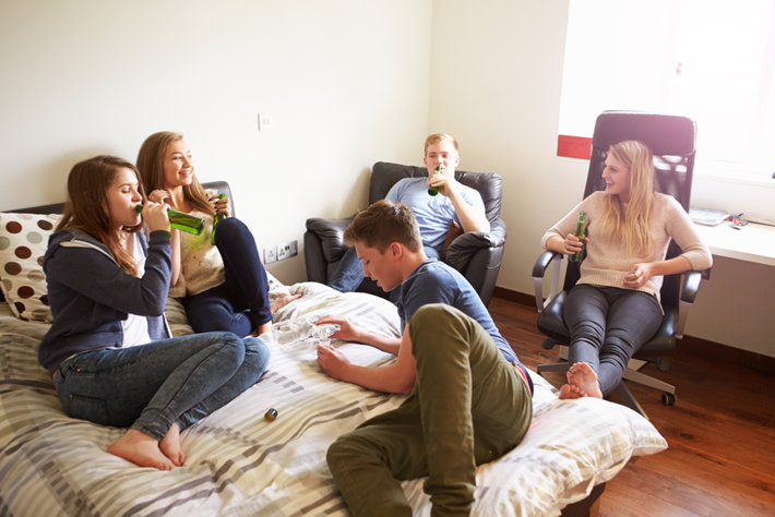 A group of teenagers is drinking alcohol in a bedroom