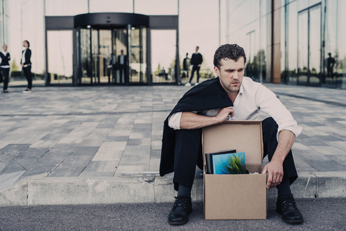 Job loss, sad man sitting in front of the company