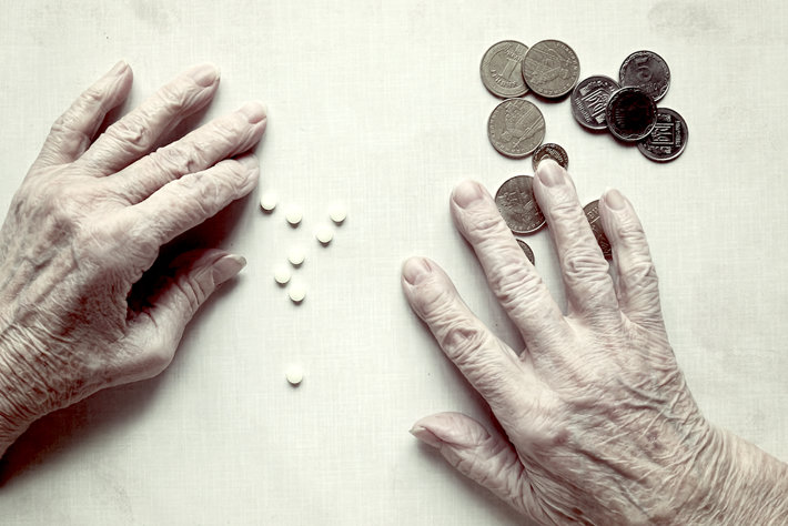 Old persons hands reaching for painkillers and money.