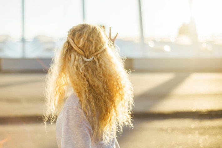 Woman with blond curly hair, standing in sunshine happy.