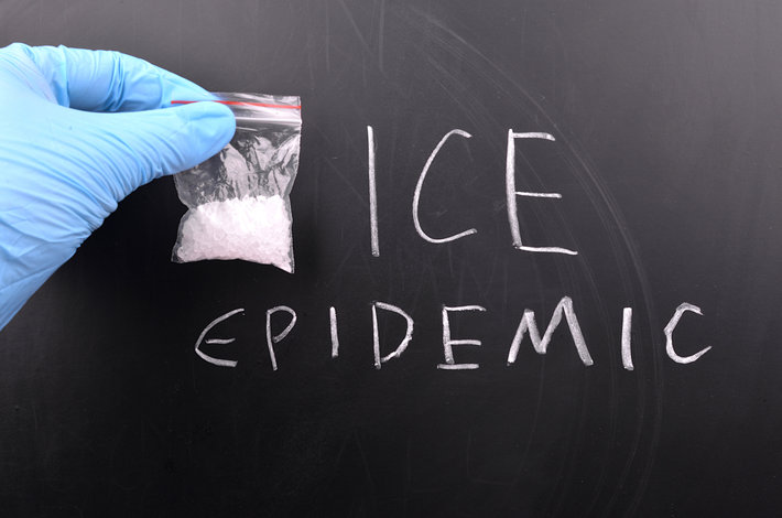Ice epidemic words on the chalkboard with a hand holding a bag of meth.