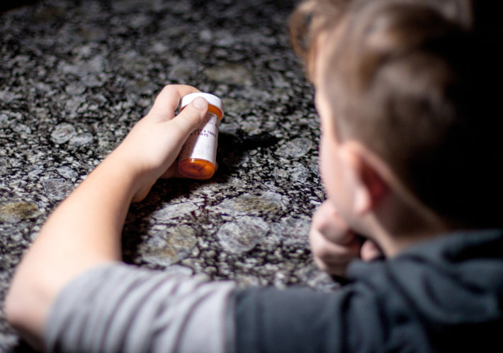 A young child looks at a pill bottle. 