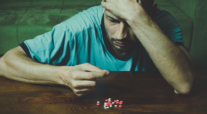 A dark photo of a man considering taking pills.